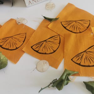 May include: Five orange fabric squares with a black printed image of a lemon wedge on each. The fabric is a mustard yellow color.