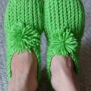 May include: A pair of green knitted slippers with a fluffy pom-pom on each toe.