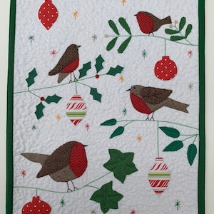 May include: A white quilted fabric panel with a green border features a Christmas scene with four red robins perched on branches with holly and ivy.  There are five red and white striped ornaments hanging from the branches.