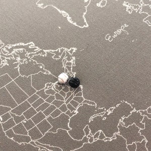 May include: A world map with two push pins, one white and one black, placed on the map of North America.