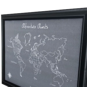 May include: A framed world map with the text "Adventure Awaits" at the top. The map is embroidered on a grey fabric background.