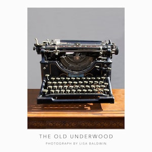 May include: A vintage black Underwood typewriter with a metal body and a brass nameplate. The typewriter is sitting on a wooden table with a carved edge.
