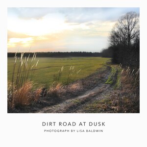 May include: A photograph of a dirt road winding through a field at dusk. The sky is a mix of yellow and blue, and the field is green. The road is lined with tall grass and trees. The text "DIRT ROAD AT DUSK" and "PHOTOGRAPH BY LISA BALDWIN" are at the bottom.