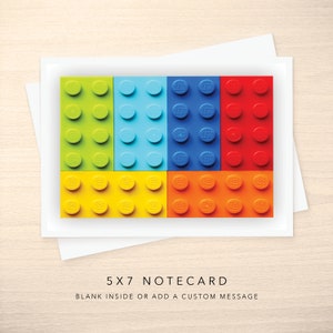 May include: A 5x7 notecard with a design of colorful LEGO bricks. The bricks are arranged in a grid pattern, with green, blue, red, yellow, and orange bricks. The notecard is blank inside, allowing for a custom message.