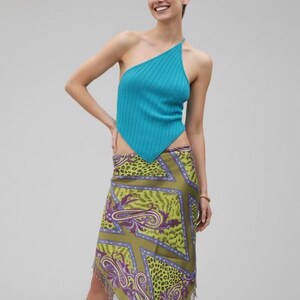 May include: A turquoise blue, one-shoulder top with ribbed texture. The skirt is a mix of green, purple, and gold, featuring paisley and leopard print patterns. The skirt has a fringed hem. Fashion apparel.