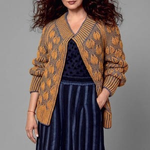 May include: A mustard yellow and gray knitted cardigan with a leaf pattern. The cardigan has long sleeves and a V-neck. The model is wearing a navy blue polka dot top and a navy blue and gray striped skirt.