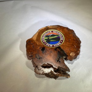 May include: A wooden coaster with a round, colorful patch that reads "Adirondack Mountains New York".
