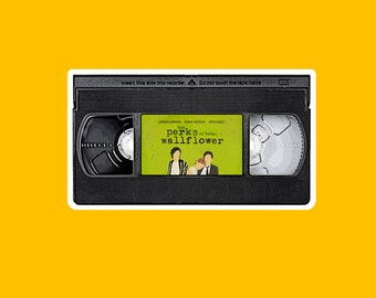 May include: A VHS tape with a black and white label. The label has the title "The Perks of Being a Wallflower" with the actors' names listed below. The tape is in a white case with a black border.