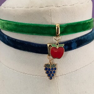 Op de afbeelding: Een tweelaagse fluwelen chokerketting met een gouden bedel met een rode appel en een tros paarse druiven.