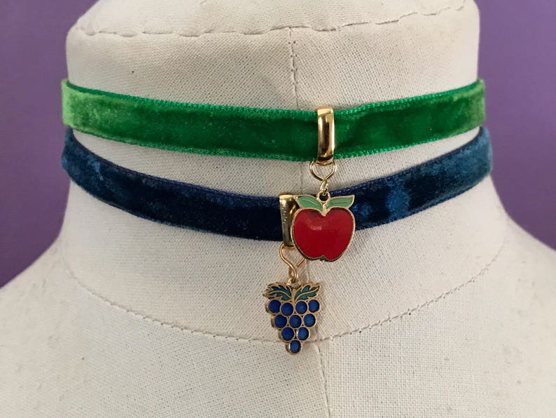 Op de afbeelding: Een tweelaagse fluwelen chokerketting met een gouden bedel met een rode appel en een tros paarse druiven.