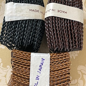 May include: Three bundles of hair accessories in black, brown, and light brown. Each bundle is wrapped with a paper band that reads "MADE IN JAPAN". The accessories appear to be made of a woven, plastic-like material.