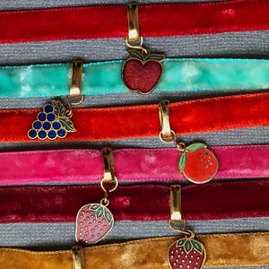Op de afbeelding: Zes fluwelen lint-choker met gouden sluitingen en ge&euml;mailleerde fruitbedels. De bedels omvatten een appel, druiven, een sinaasappel en twee aardbeien.