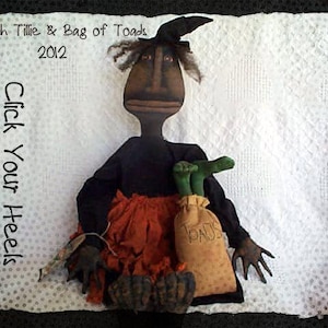 May include: A black witch doll with a green hat and a bag of toads. The doll is wearing a black dress and a red skirt. The doll is holding a bag that says "Toads" on it. The text "Witch Tillie & Bag of Toads 2012" and "Click Your Heels" is visible in the image.