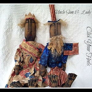 May include: Two rag dolls dressed as Uncle Sam and Lady Liberty. The dolls are wearing red, white, and blue clothing and have a patriotic theme. The text "Click Your Heels" is visible in the background.