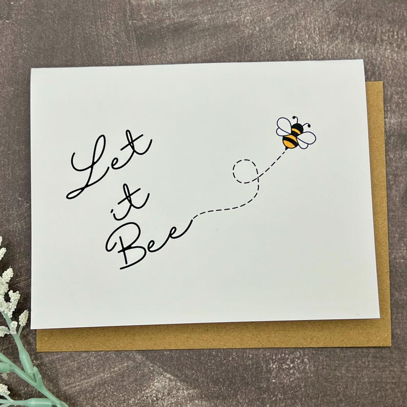May include: A white card with the words "Let it Bee" in black script. A cartoon bee with yellow and black stripes flies to the right, with a dotted line. The card is on a brown envelope.