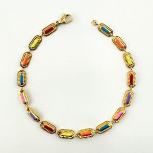 Könnte beinhalten: Goldfarbenes Armband mit bunten Emaille-Akzenten. Das Armband hat eine Reihe von rechteckigen Gliedern, jedes mit einer anderen Farbe, darunter Rot, Orange, Gelb, Grün, Blau und Lila. Das Armband wird mit einem Karabinerverschluss befestigt.