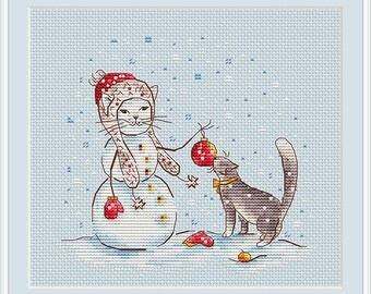 May include: A white cat wearing a red and white hat is dressed as a snowman. The cat is holding a red ornament and looking at a gray cat with a red bow. The cats are standing on a blue background with white snowflakes.