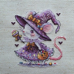 Könnte beinhalten: Eine Kreuzstichstickerei auf hellbeigem Stoff, die eine als Hexe verkleidete Maus zeigt. Die Maus trägt einen violetten Hut mit gelber Schleife und ein violettes Kleid mit einem Kürbiseimer. Sie hält einen gestreiften Lutscher, umgeben von kleinen Fledermäusen.