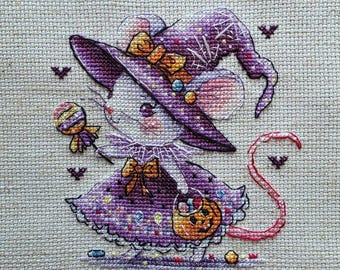 May include: A cross-stitch embroidery on light beige fabric featuring a mouse dressed as a witch. The mouse wears a purple hat with a yellow bow and a purple dress with a pumpkin bucket. It holds a striped lollipop, surrounded by small bats.