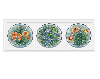 Puede incluir: Tres diseños de bordado circulares con diferentes arreglos florales. El primer diseño muestra un ramo de rosas naranjas con hojas verdes. El segundo diseño muestra un ramo de flores azules con hojas verdes. El tercer diseño muestra un ramo de lirios naranjas con hojas verdes.