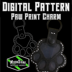 May include: A black leather paw print charm keyring with white stitching, a central snap button, and a metal ring. The text reads DIGITAL PATTERN PAW PRINT CHARM and MOONSHINE BESPOKE WORKS. A line art outline of the paw print design is visible behind the charm.