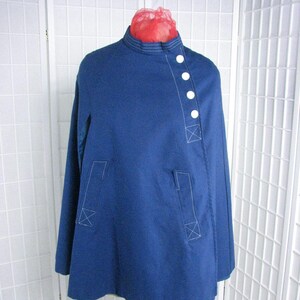 May include: A blue cape with white buttons and white stitching. The cape has a high collar and is made of a thick fabric.