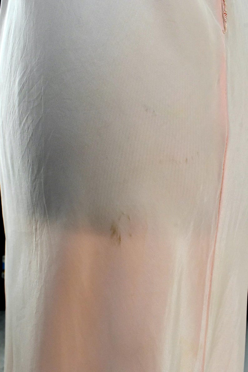 May include: Pale pink, sheer fabric garment with a vertical seam and delicate trim. The fabric appears to be slightly wrinkled, with some darker areas and brown spots. The garment's design is simple and elegant.