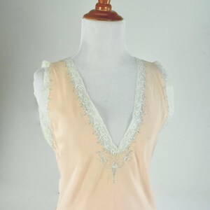 May include: A peach-colored, sleeveless slip dress with a V-neckline. The neckline and armholes are trimmed with white lace. The dress is displayed on a mannequin.