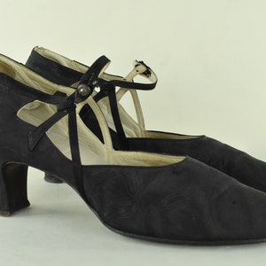 May include: A pair of black satin heeled shoes with a criss-cross strap and buckle detail.