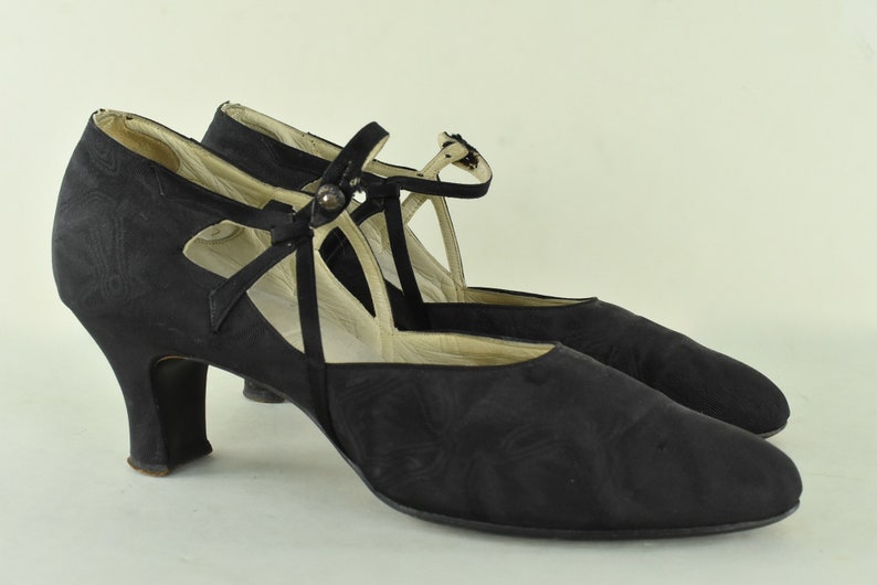 May include: A pair of black satin heeled shoes with a criss-cross strap and buckle detail.