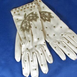 May include: A pair of white gloves with gold embroidery and small gold studs. The gloves are made of a soft, delicate fabric.