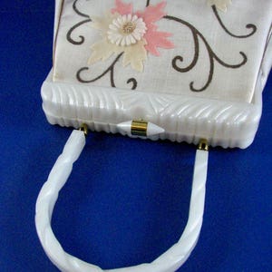 May include: White vintage handbag with a white plastic handle and a floral design on the front. The flowers are pink, white, and blue.