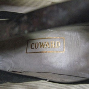 May include: Close-up of the inside of a black leather shoe with a white label that reads "COWARD".