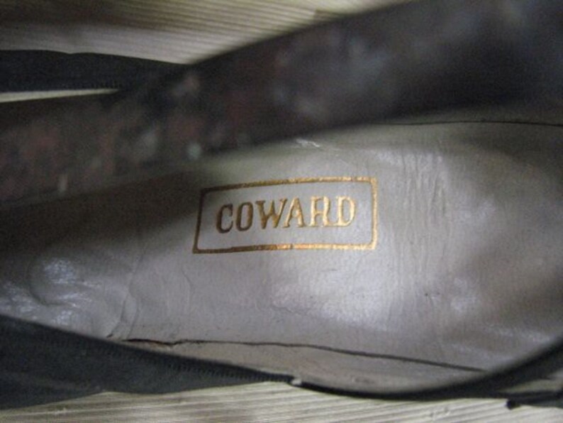 May include: Close-up of the inside of a black leather shoe with a white label that reads "COWARD".