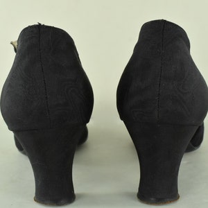 May include: A pair of black heeled shoes with a closed toe and a buckle strap. The shoes have a low block heel.
