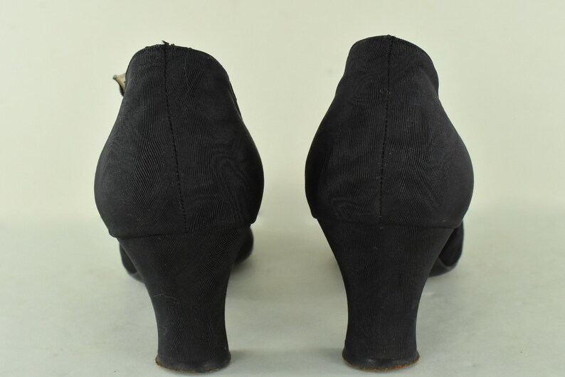 May include: A pair of black heeled shoes with a closed toe and a buckle strap. The shoes have a low block heel.