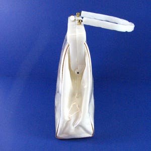 May include: A white plastic handbag with a gold-tone handle. The bag has a rectangular shape and a smooth, glossy finish.