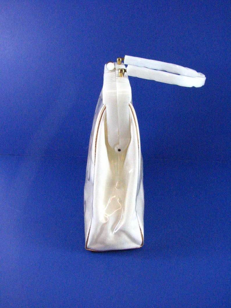 May include: A white plastic handbag with a gold-tone handle. The bag has a rectangular shape and a smooth, glossy finish.