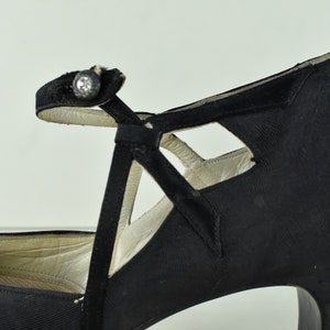 May include: Black satin high-heeled shoes with a cut-out design and a single buckle strap.