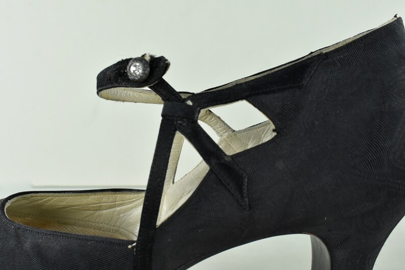 May include: Black satin high-heeled shoes with a cut-out design and a single buckle strap.