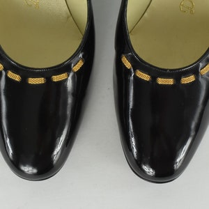Könnte beinhalten: Paar schwarze Lackleder-Ballerinas mit goldfarbenem Besatz am oberen Rand. Die Schuhe haben eine runde Spitze und ein glänzendes Finish, geeignet für formelle oder halbformelle Anlässe.