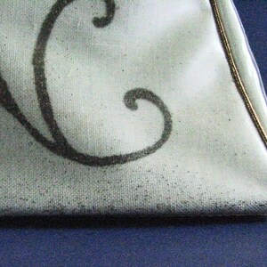 May include: A white fabric bag with a black floral design and a gold trim around the edge.
