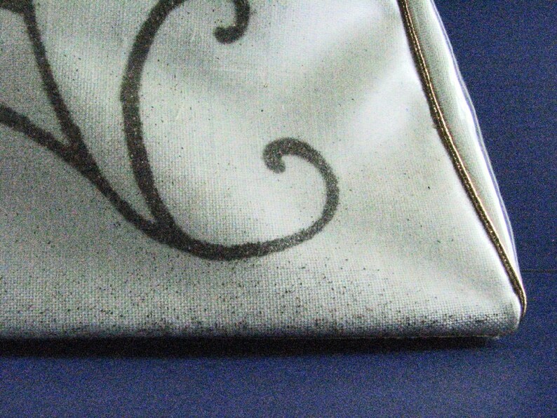 May include: A white fabric bag with a black floral design and a gold trim around the edge.
