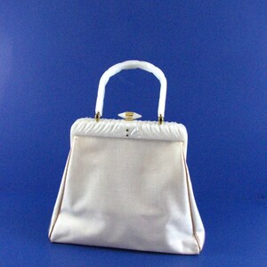 May include: A white vintage handbag with a white plastic handle and a gold clasp. The bag has a textured fabric exterior.