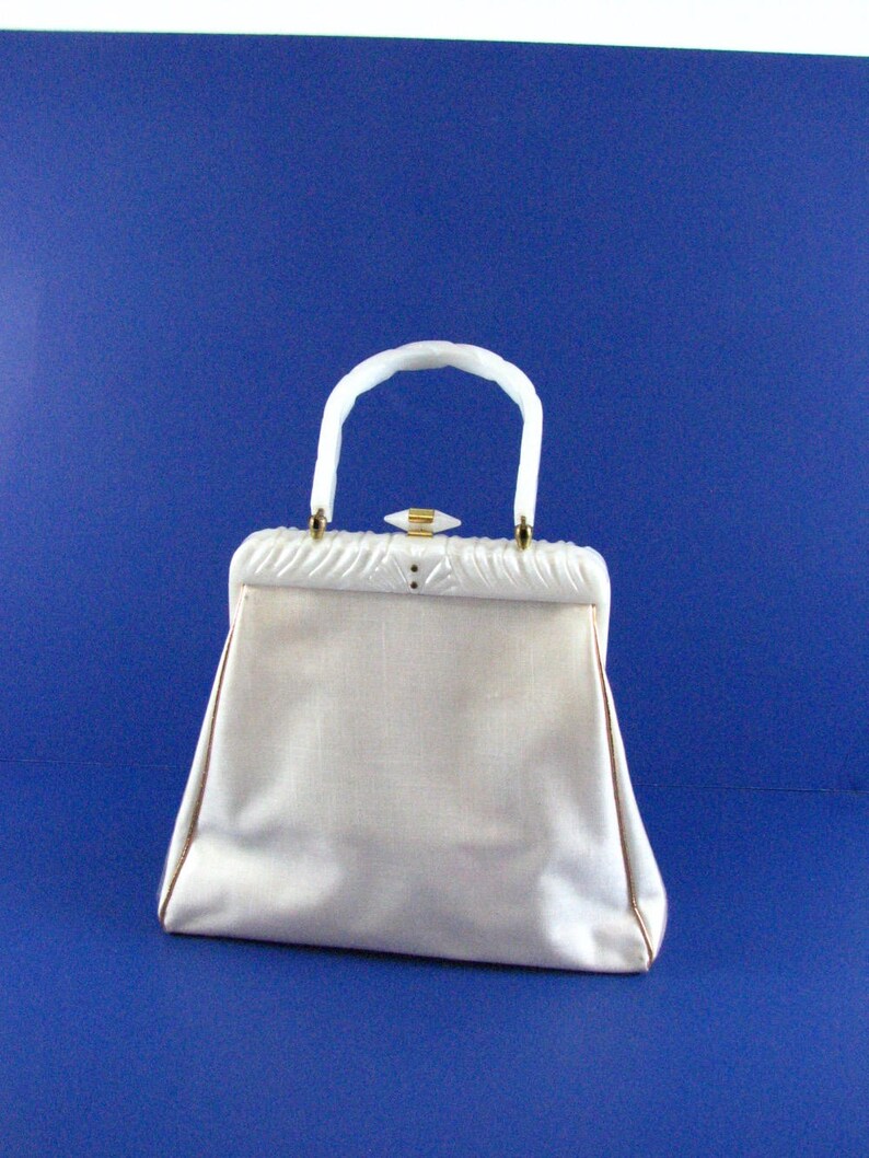 May include: A white vintage handbag with a white plastic handle and a gold clasp. The bag has a textured fabric exterior.