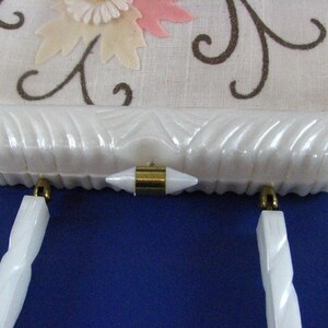 May include: A white vintage clutch purse with a floral design and gold-tone hardware. The purse has a white, textured exterior and two white handles.