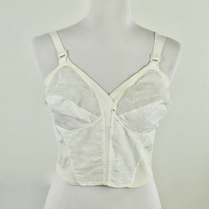 May include: A vintage white bra with adjustable straps and a front closure. The bra features a delicate floral lace design on the cups and a smooth, satin-like fabric on the body. The bra is displayed on a mannequin.