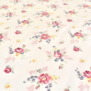 May include: Cream-colored fabric with a repeating floral pattern. The design features clusters of pink and red roses, small yellow flowers, and blue accents. The overall effect is a delicate, vintage-inspired print.