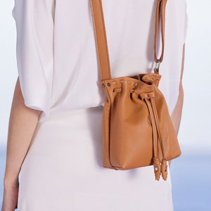 Brown Leather small bucket bag beautifully handcrafted in Greece. The boho small purse features a drawstring closer with an adjustable shoulder strap. You can easily wear it crossbody too. It protects your cellphone in its interior pocket