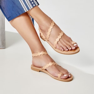 May include: A pair of light brown leather sandals with a scalloped edge design. The sandals have a thong toe and ankle straps.